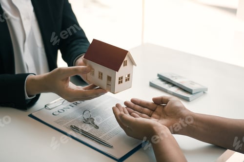 Preview: Real estate agent congratulations to new buyer by giving house model to client in the agency office.