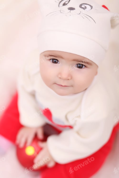Preview: baby girl in Santa Claus hat with gifts under Christmas tree