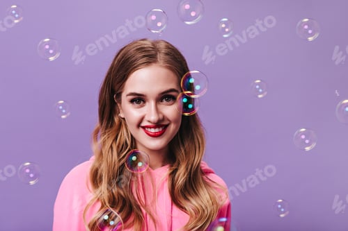 Preview: Portrait of lady in pink outfit posing on purple background with bubbles. Pretty cheerful blonde wo
