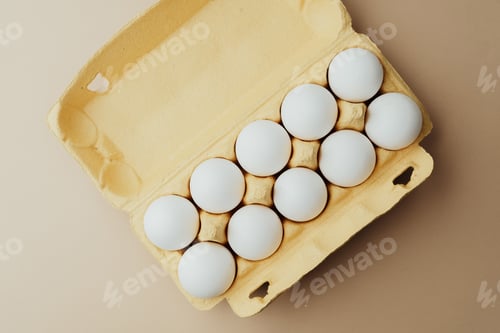 Preview: White eggs in yellow carton top view on beige background