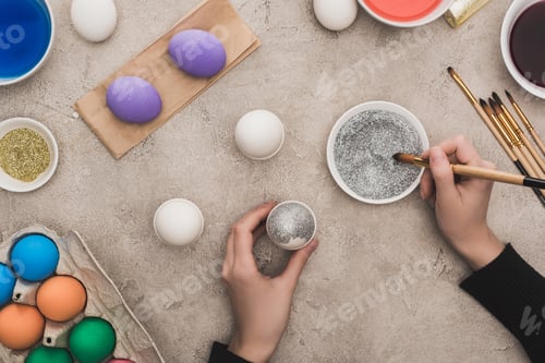 Preview: cropped view of woman decorating chicken eggs with silver glitter on grey concrete surface