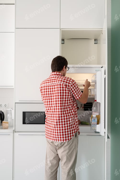 Preview: Young man holding disposable plastic boxed with food and putting them to the fridge