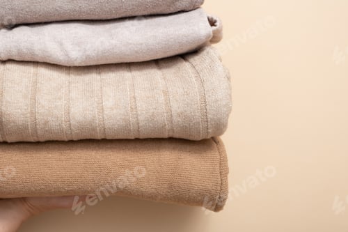 Preview: A stack of cozy knitted sweaters in women's hands on beige background. Warm concept