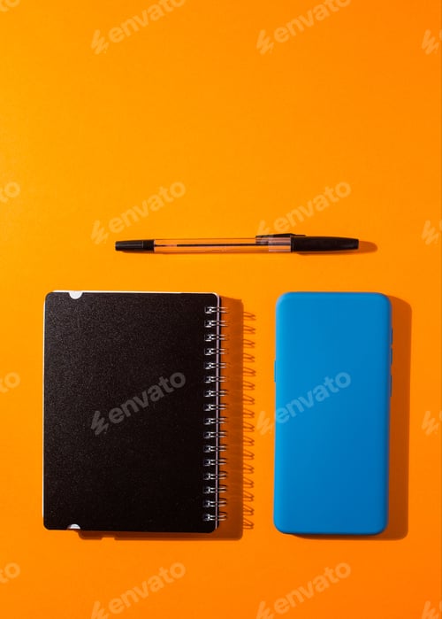 Preview: Vertical shot of a smartphone and a notepad with a pen on an orange background