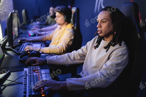 Vista previa: Jugador multirracial jugando a un videojuego en el ordenador cerca de un equipo borroso en un ciberclub