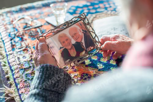 Preview: Elderly hands holding a treasured photo frame with an image of an older couple
