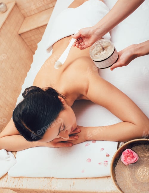Preview: Beautiful brunette woman during body peeling at the spa. Enjoys skin peeling, skin cleansing, and