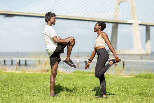 Preview: Two friends stretching together at a park near a river during daytime