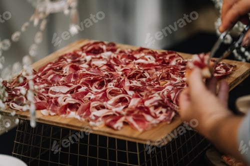 Preview: Closeup of a person taking a piece of the sliced delicious Iberian ham on the wooden board