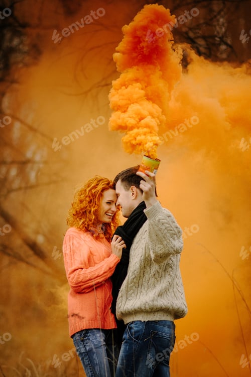 Preview: Young happy couple holding smoke bombs on camping