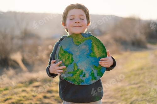 Preview: Little boy holding planet in hands against green spring background. Earth day