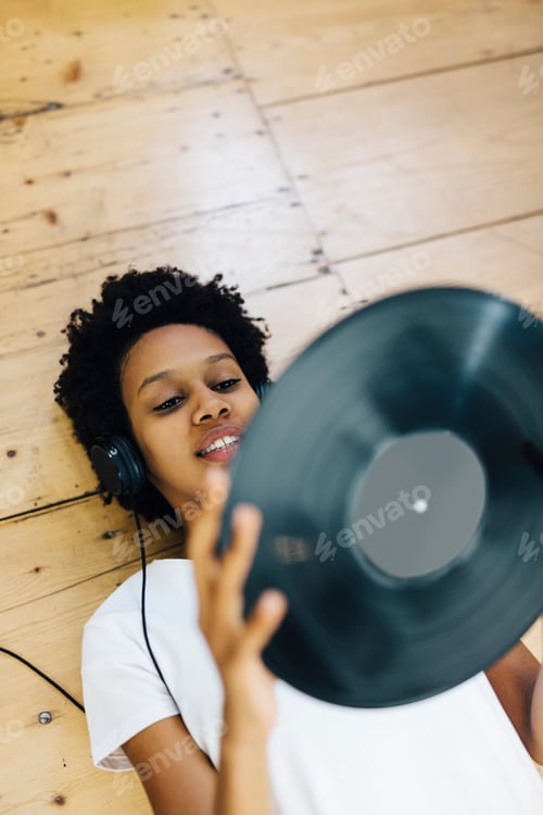 Preview: Young woman at home listening vinyl records, lying on ground