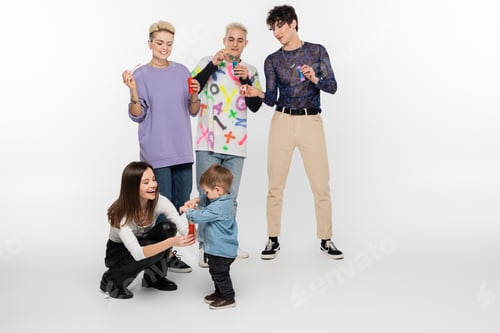 Preview: happy lgbtq friends blowing soap bubbles near toddler boy on grey background