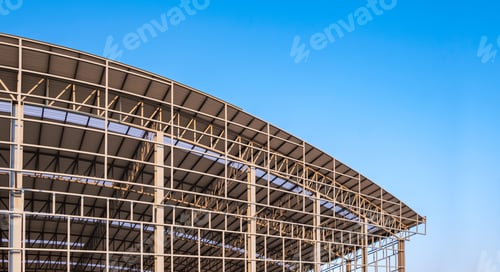 Preview: Part of large metal factory building structure in construction site against blue sky background