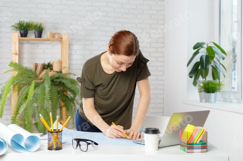 Preview: Woman draws on paper at desk with plants and laptop during daytime work hours