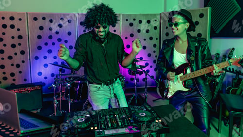 Preview: Young happy people playing music with dj mixer and guitar in house production studio