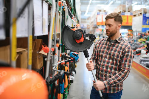 Preview: happy customer with electric lawn trimmer in hands at garden equipment store