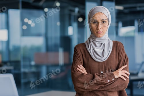 Preview: Serious and focused businesswoman in hijab and glasses looking at camera with crossed arms, working