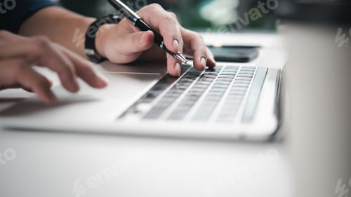 Preview: Hands typing on laptop keyboard, pen in hand, emphasizing productivity, digital work. Ideal for offi