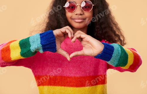 Preview: Happy ethnic girl in trendy sunglasses showing heart gesture