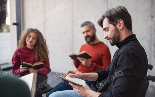 Preview: Men and women sitting in circle reading Bible book during group therapy