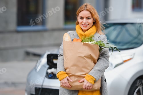 Preview: Girl stands near her electric car and waits when vehicle will charged.