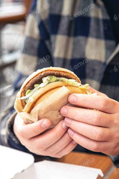 Preview: Burger in male hands close-up in a fast food cafe.
