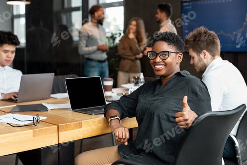 Preview: African American businesswoman sitting at desk showing thumbs up gesture