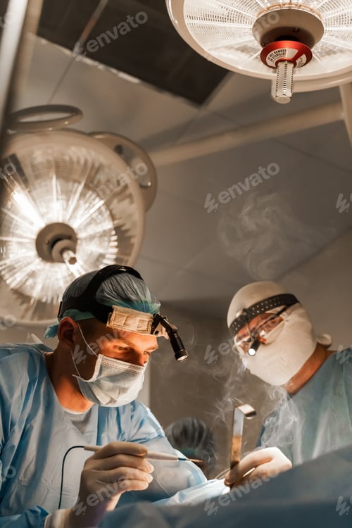 Preview: Two surgeons operate with headlamp on breast enhancement procedure in clinic.