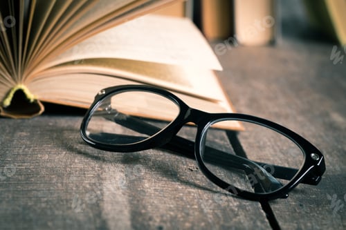 Preview: Eyeglasses Resting on Open Book on Wood Table