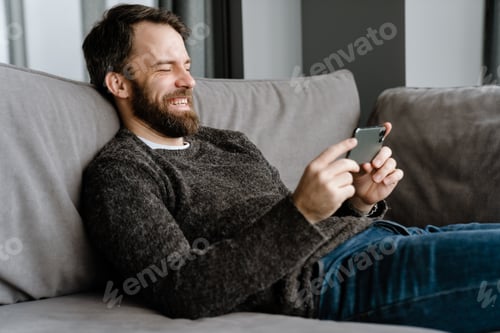 Preview: Bearded european man using mobile phone while sitting on sofa