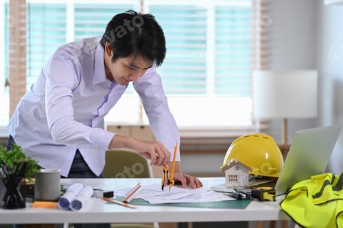 Preview: Asian male construction engineer working with blueprint in office.