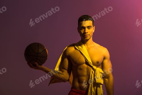 Preview: handsome sportive mixed race man holding brown ball on purple background
