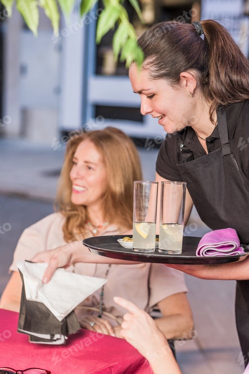 Preview: latin waitress woman smiling serving food in restaurant to a mature group of friends together.