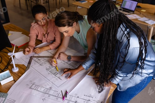 Preview: Diverse female architects in discussion using blueprints in casual office meeting