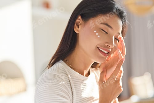 Preview: Skincare Routine. Smiling Woman Applying Skincare Cream to Smooth Face in Natural Light