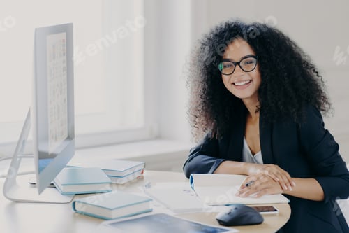 Preview: Glad curly office worker watches webinar on business topic, writes down notes with pen