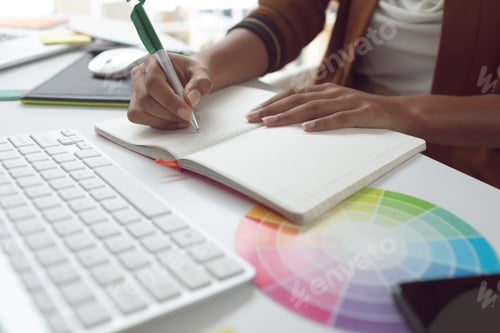 Preview: Mid section of Asian female graphic designer writing on diary at desk in a modern office