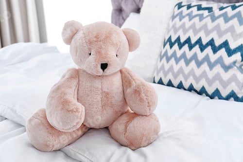 Preview: Cute teddy bear sitting on bed indoors. Space for text