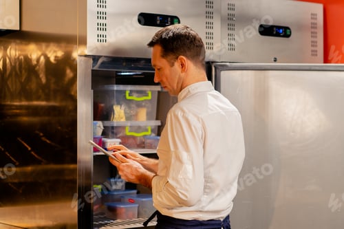 Preview: professional kitchen chef looks into the fridge and chooses ingredients for cooking food concept