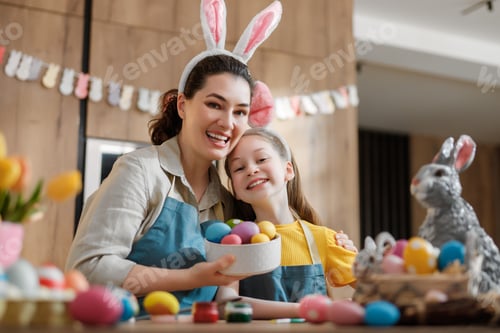 Vista previa: Familia feliz celebrando la Pascua en casa: madre e hija pintan huevos de colores