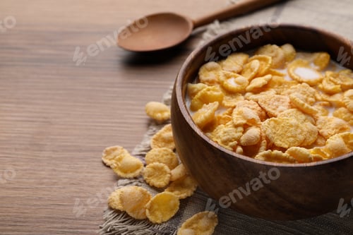 Preview: Tasty cornflakes with milk in bowl served on wooden table, closeup. Space for text