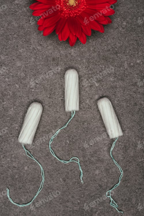 Preview: top view of arranged menstrual tampons and red flower on grey surface