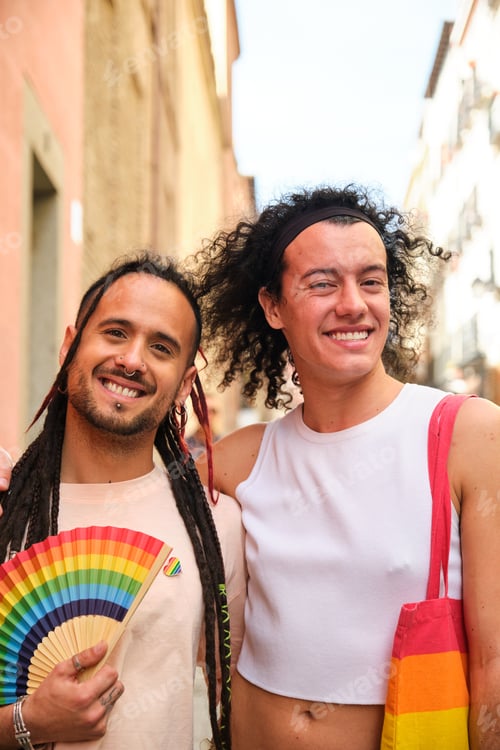 Preview: Gay couple smiling, looking at camera and holding a rainbow fan.