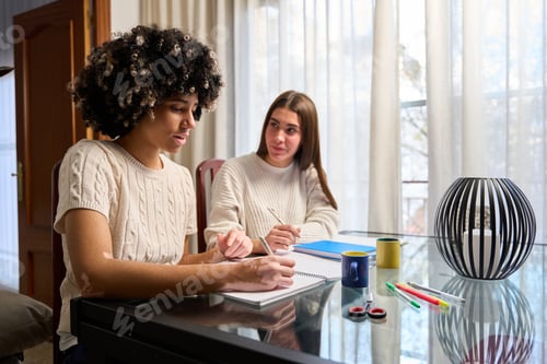 Preview: Female students taking notes and studying together at home