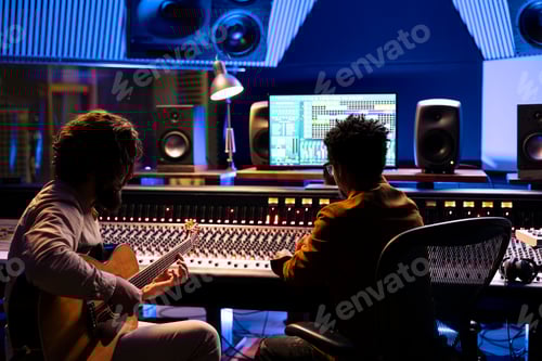 Preview: Artist playing electro acoustic guitar in control room at studio,