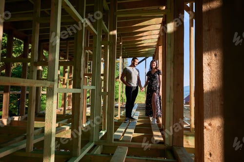 Preview: Man and woman inspecting their future wooden frame house nestled in the mountains near forest.