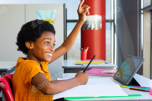 Preview: Happy biracial schoolboy having lesson on tablet video call in classroom