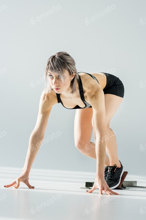 Preview: Attractive young sportswoman in starting position on grey