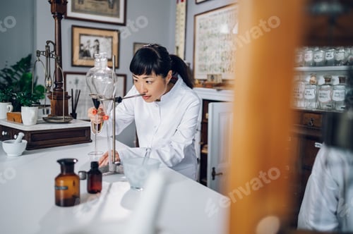 Preview: A focused Japanese pharmacist is making medicine by using a funnel